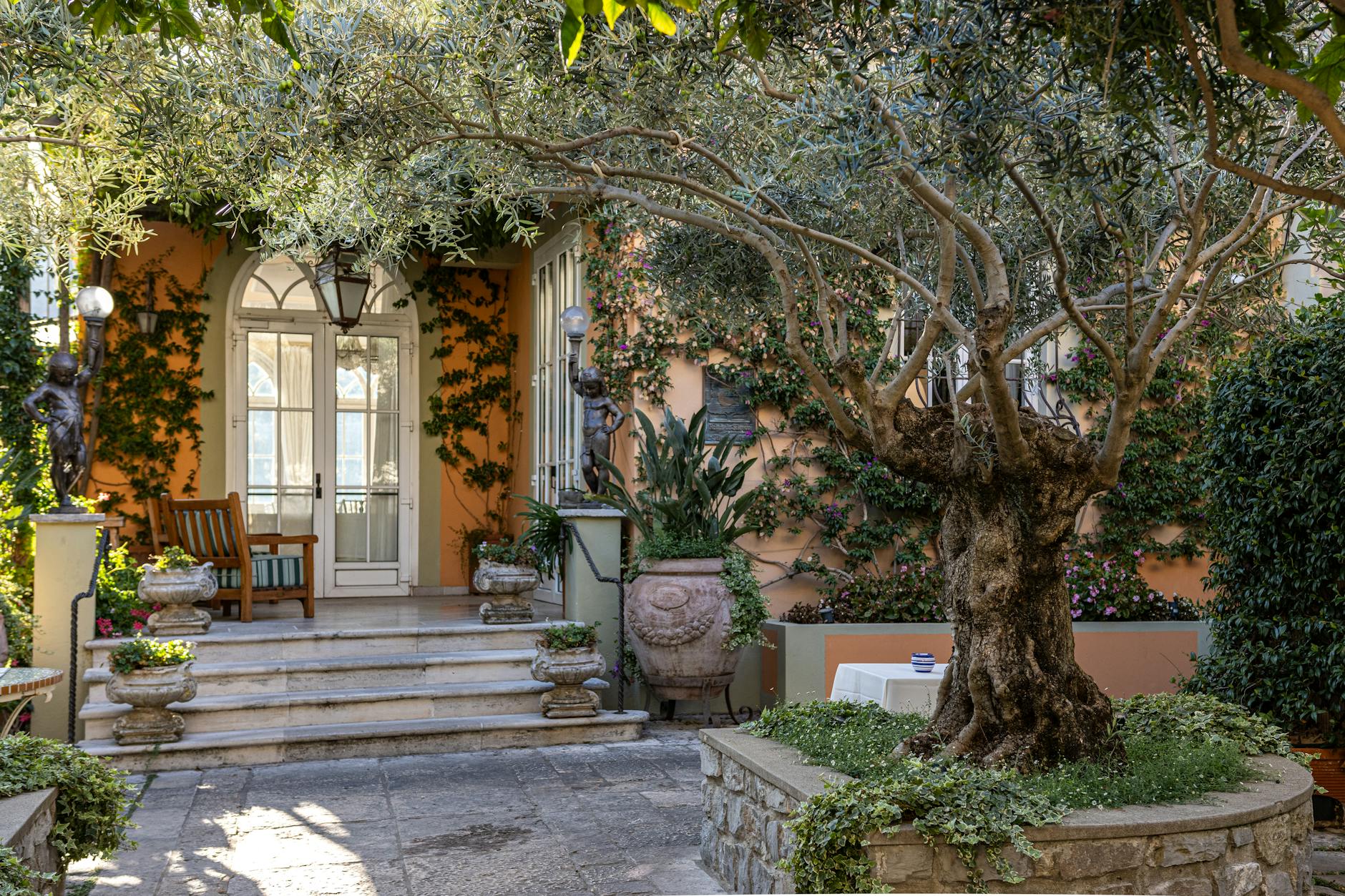 Elegant Mediterranean villa entrance with lush greenery and classic decor.